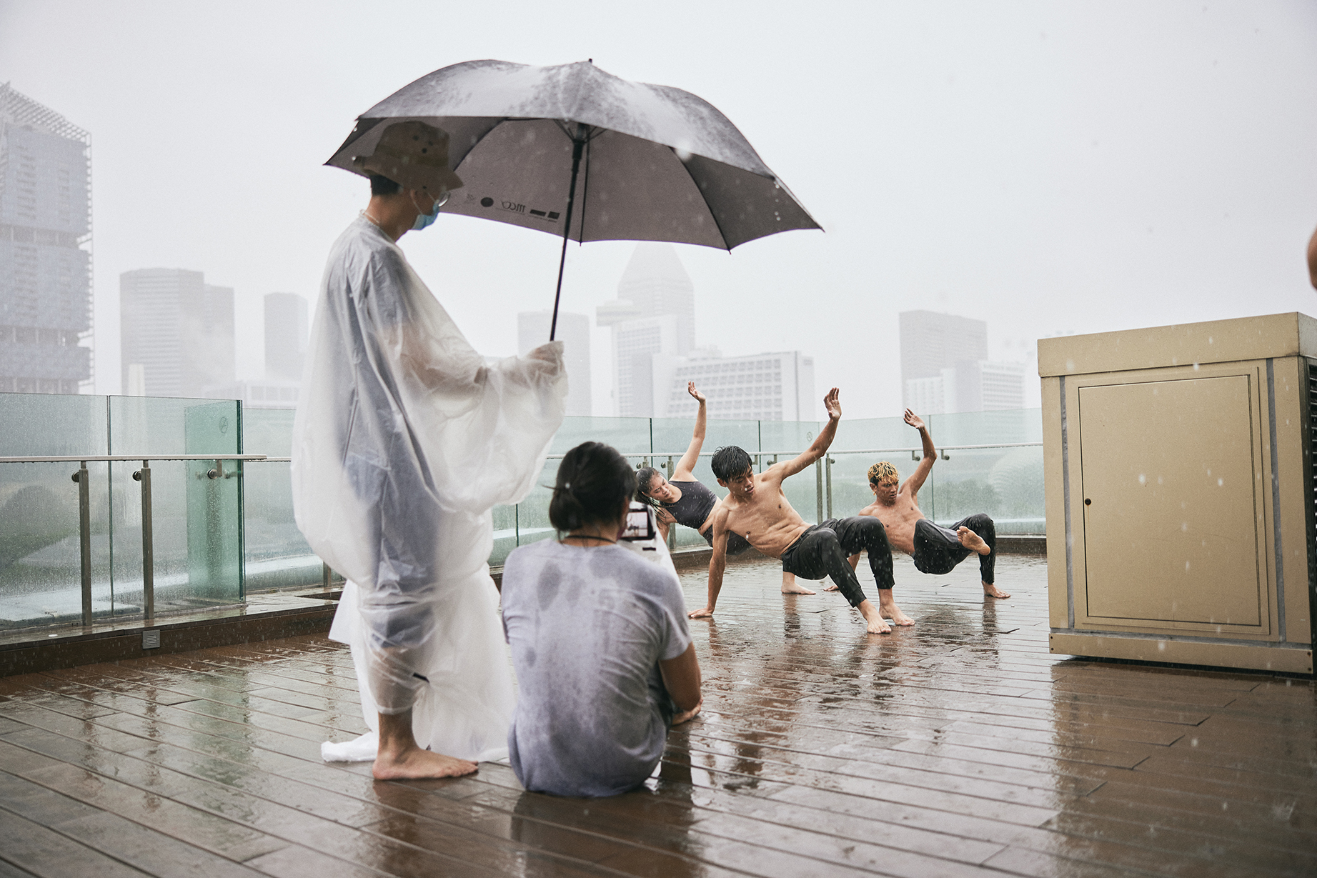 Choreographer Yarra Ileto monitors the filming, clad in a raincoat under an umbrella.