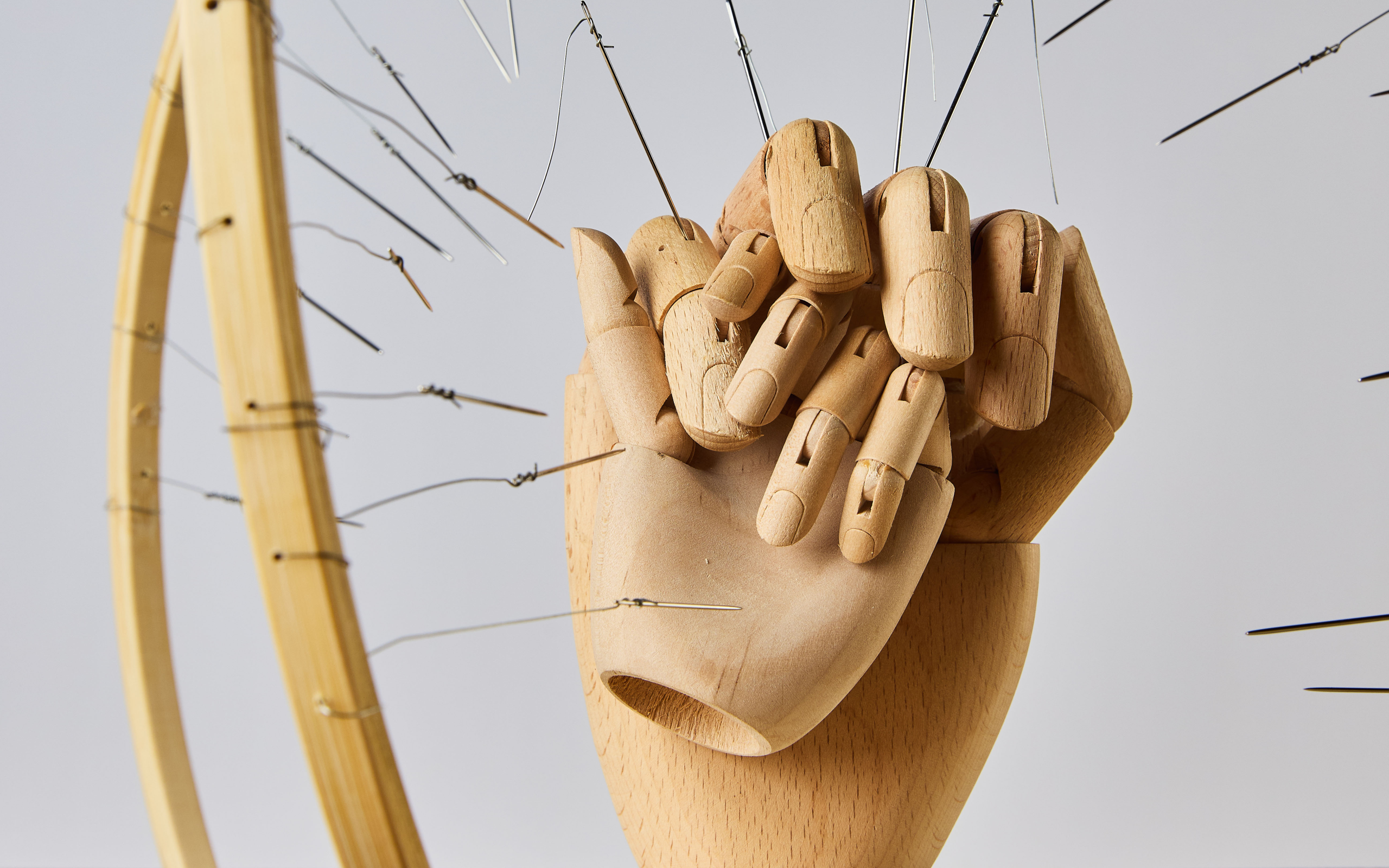Close-up of two wooden mannequin hands interlocked, surrounded by curved wood and metal wires in a tactile sculptural art piece.