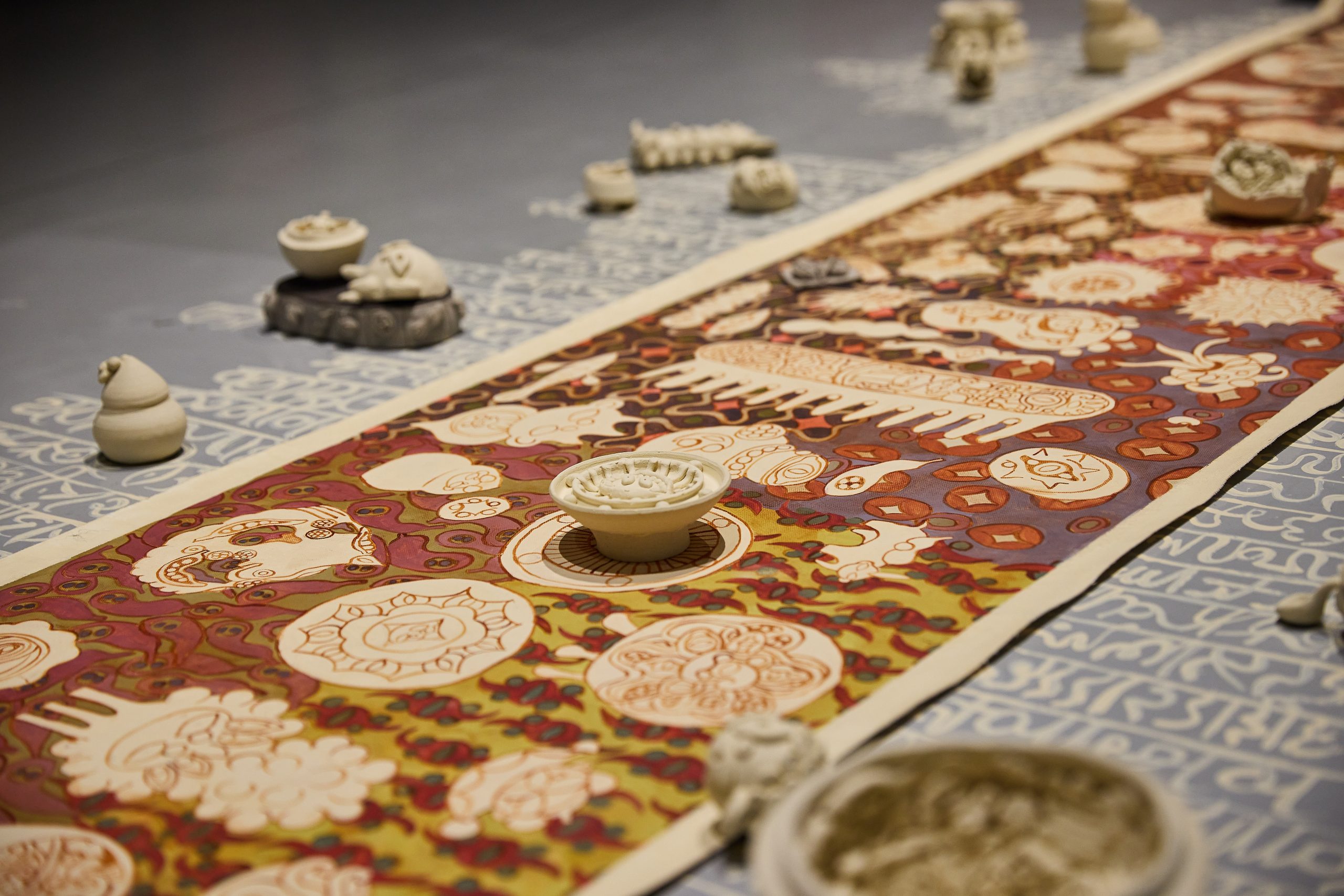Close-up of an art installation with a vibrant hand-painted textile, ceramic vessels, and calligraphic patterned backdrop.