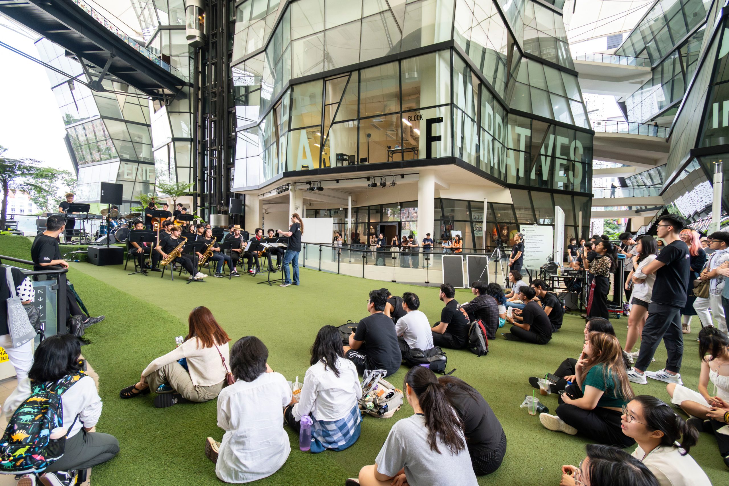 Modern glass façade of LASALLE’s McNally Campus with sky bridges and white canopy roof, framing an open courtyard view.