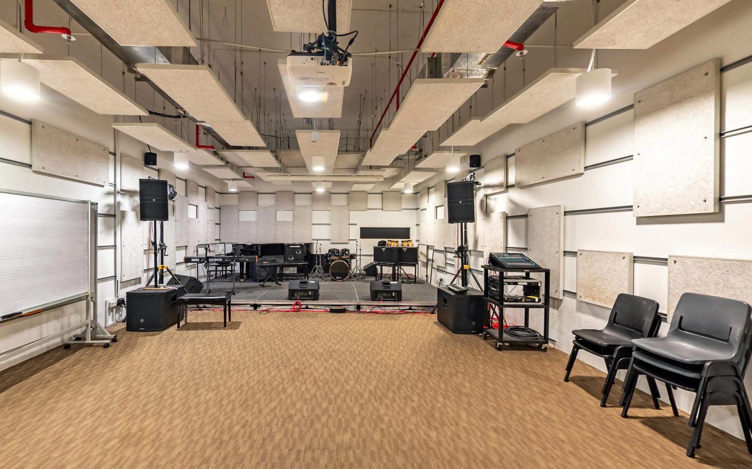 Spacious soundproof studio with drum kit, piano, mixing desk and ceiling-mounted acoustic panels.