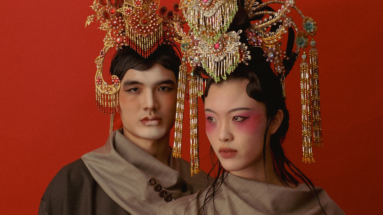 Two individuals in draped garments wearing elaborate gold and red headpieces, posed against a red backdrop with dramatic styling.