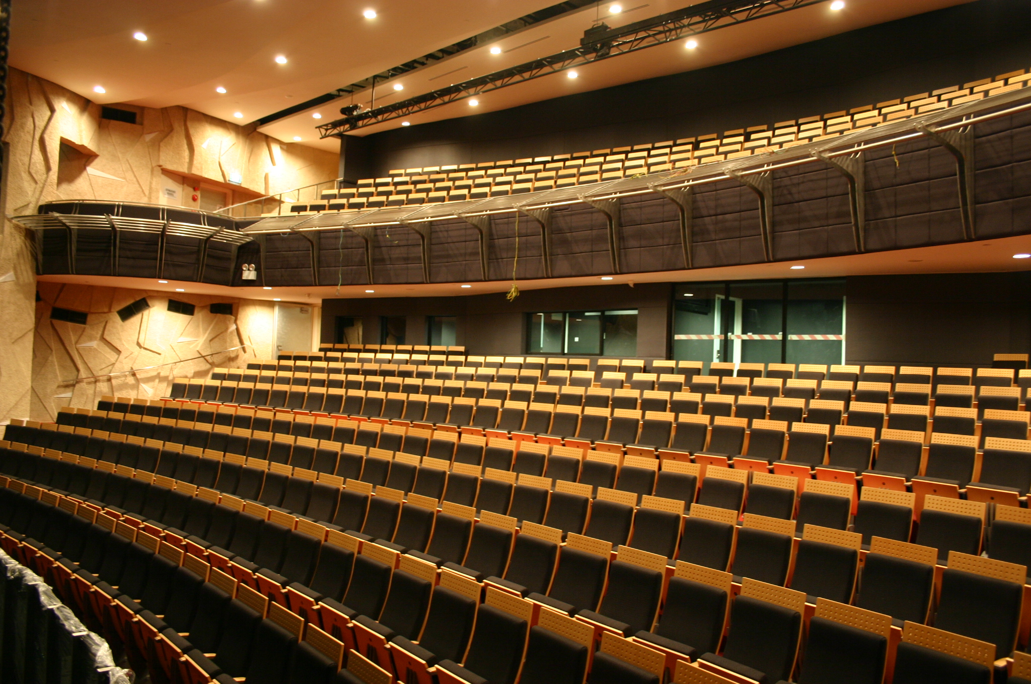 View of an empty auditorium with tiered seating, acoustic panelled walls and a balcony overlooking the main floor.