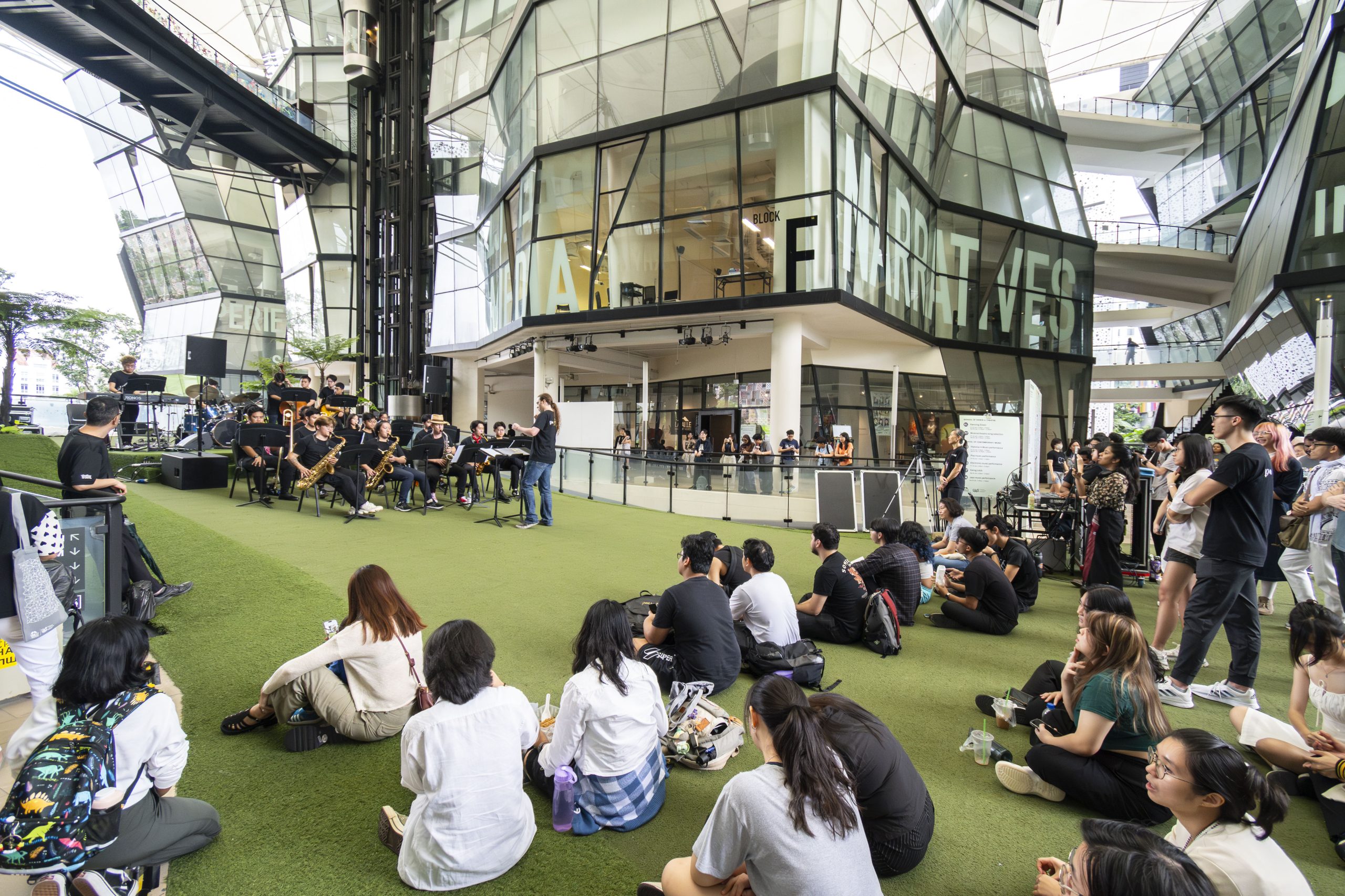 Students sit on the Campus Green under LASALLE’s glass buildings, watching a live jazz ensemble perform.