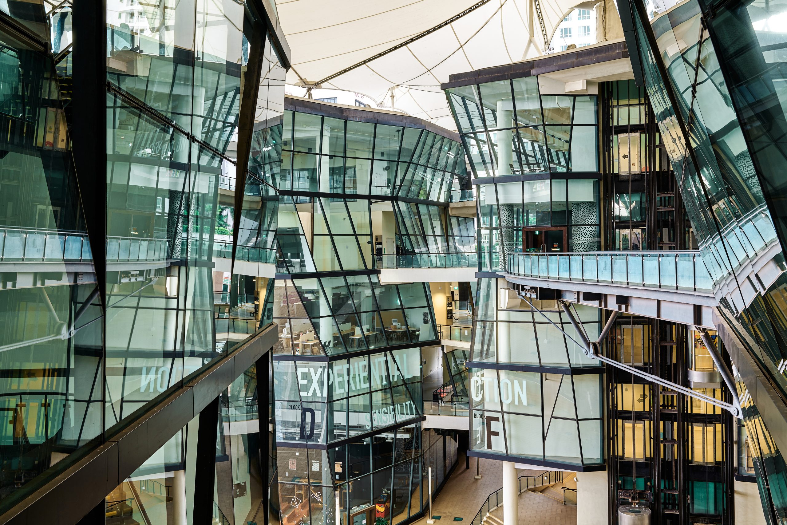 Interior view of LASALLE’s McNally Campus showing angular glass buildings with elevated walkways and visible words like “EXPERIENTIAL” and “CONNECTION” on the façades.