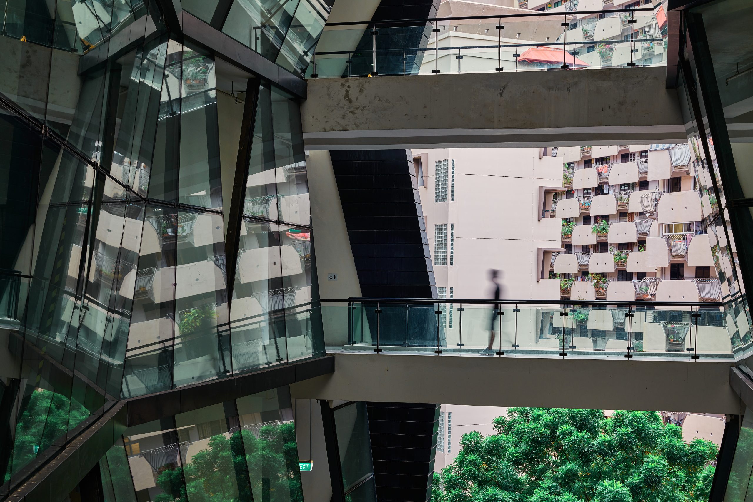 Silhouette of person walking across glass bridge, framed by angular reflections and city block seen through LASALLE campus windows.