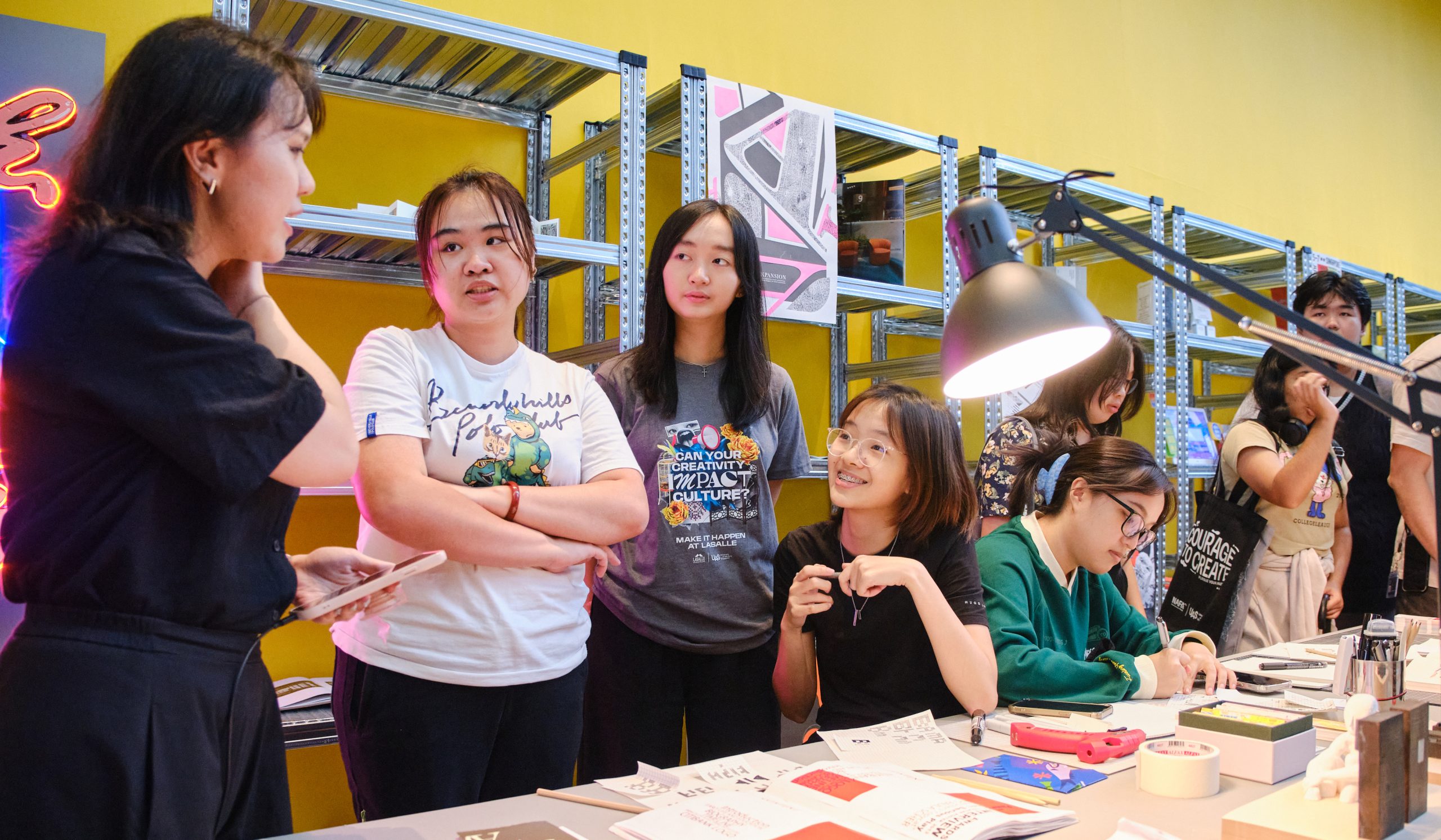 Students engaging in discussion and creative activities at a brightly lit table, surrounded by tools, zines and printed materials.