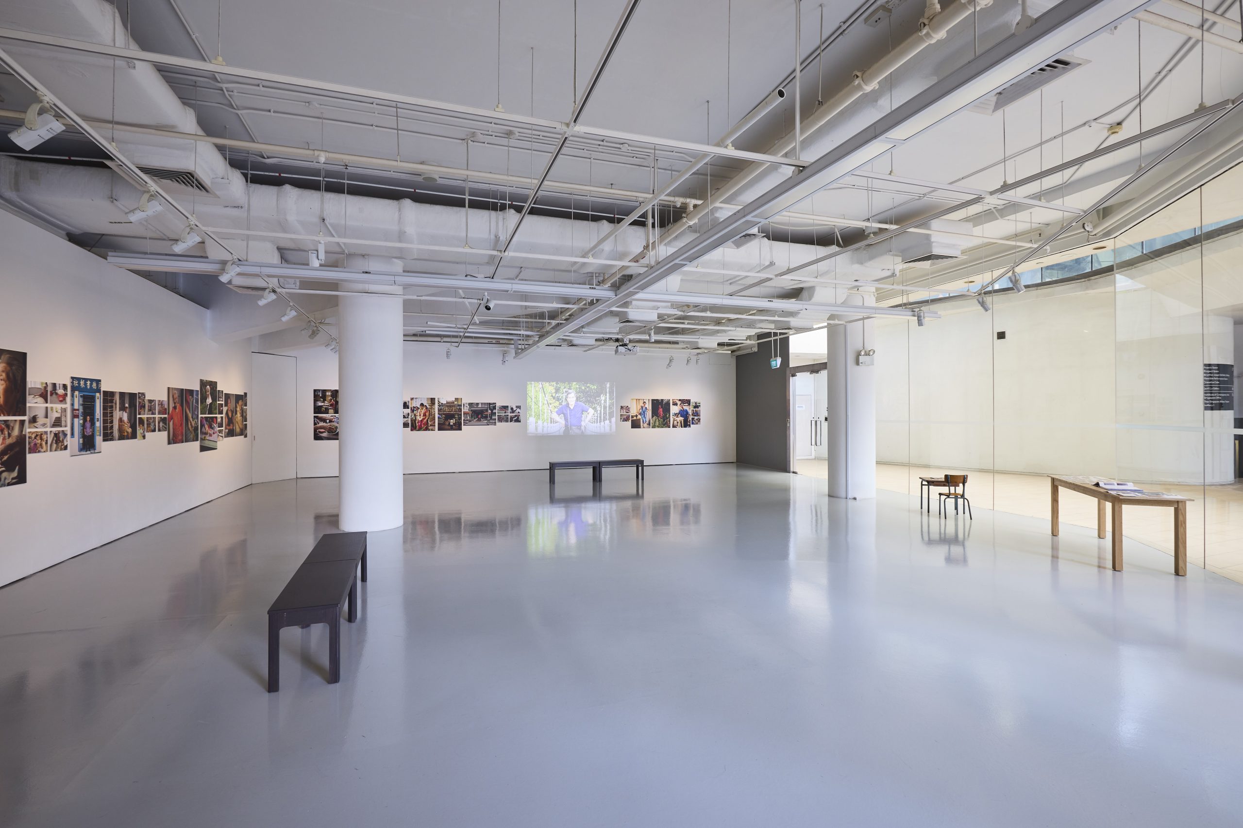 Bright LASALLE gallery with photo series displayed on white walls, benches in the centre and a projected video at the far end.