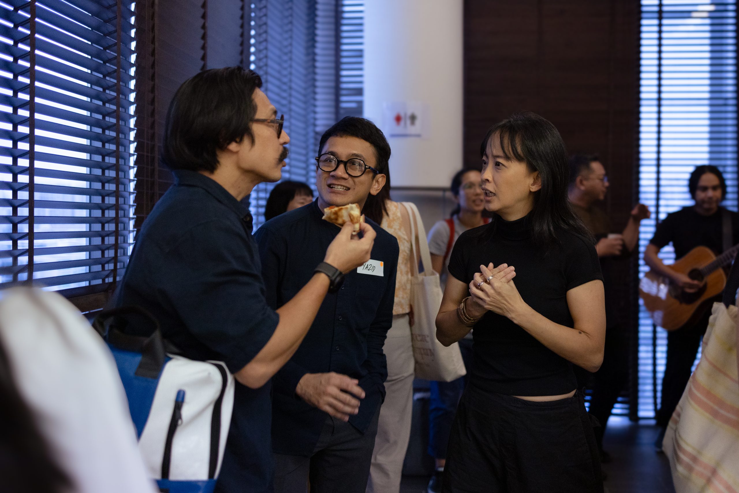 A man gestures while speaking with a woman at a LASALLE gallery, with other visitors chatting near wall art and glass windows.