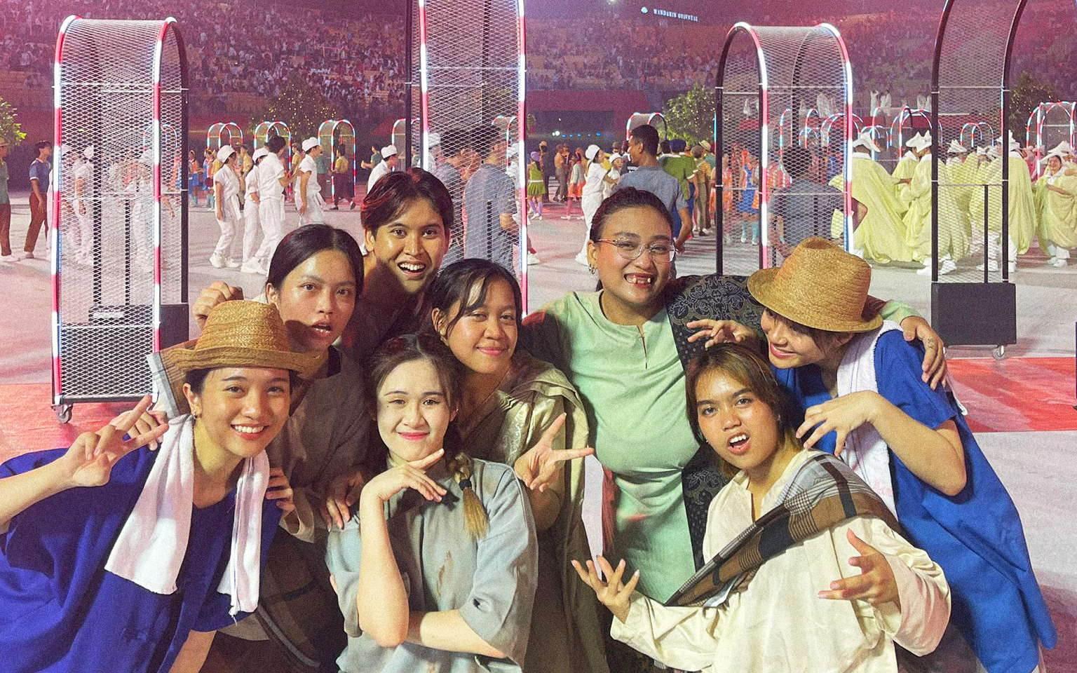 Group of LASALLE performers in costume posing cheerfully at a large-scale event with a festive crowd and stage props behind them.