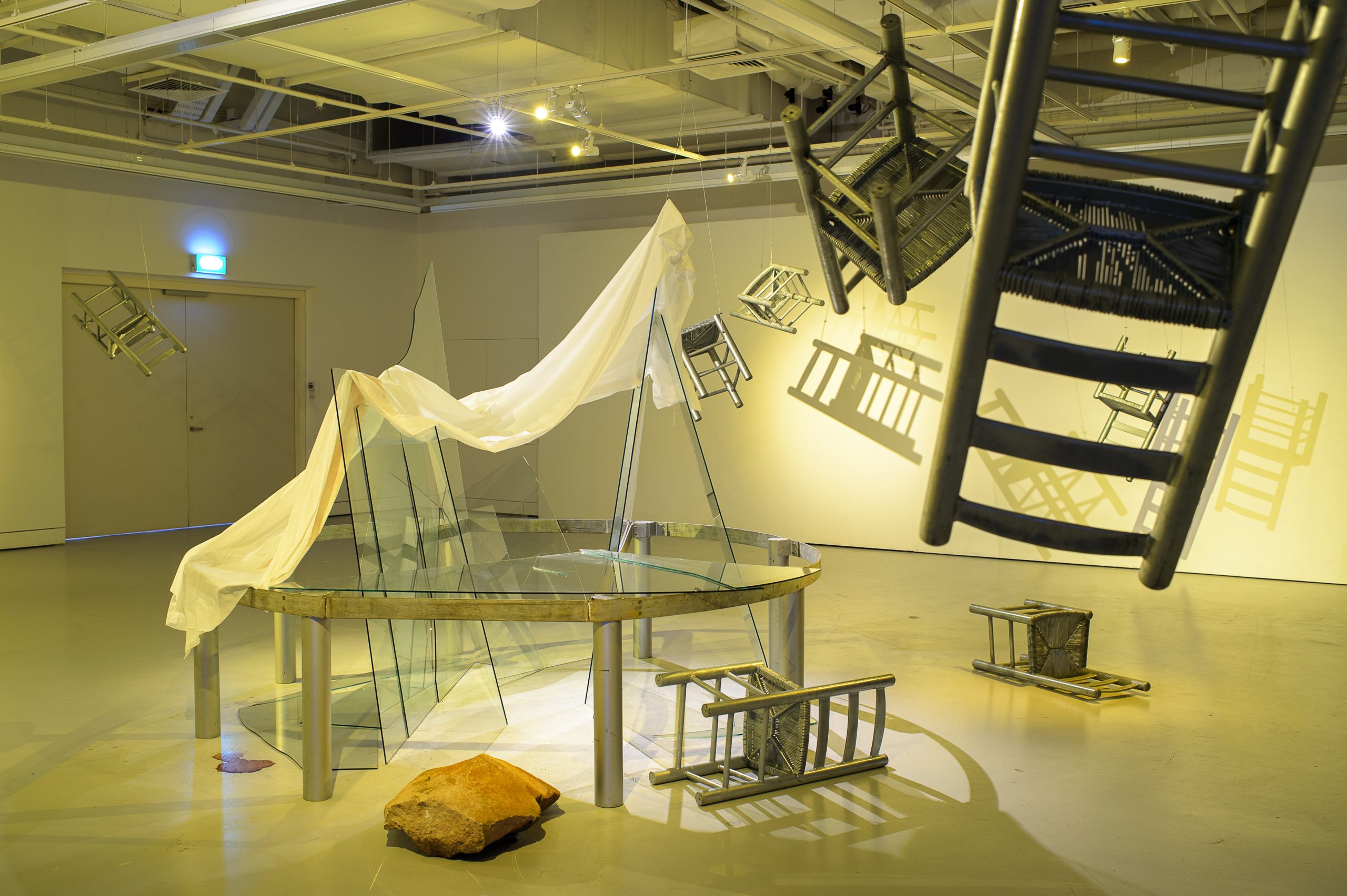 LASALLE installation of suspended chairs casting shadows, with glass panels, fabric and stone arranged in a sculptural display.