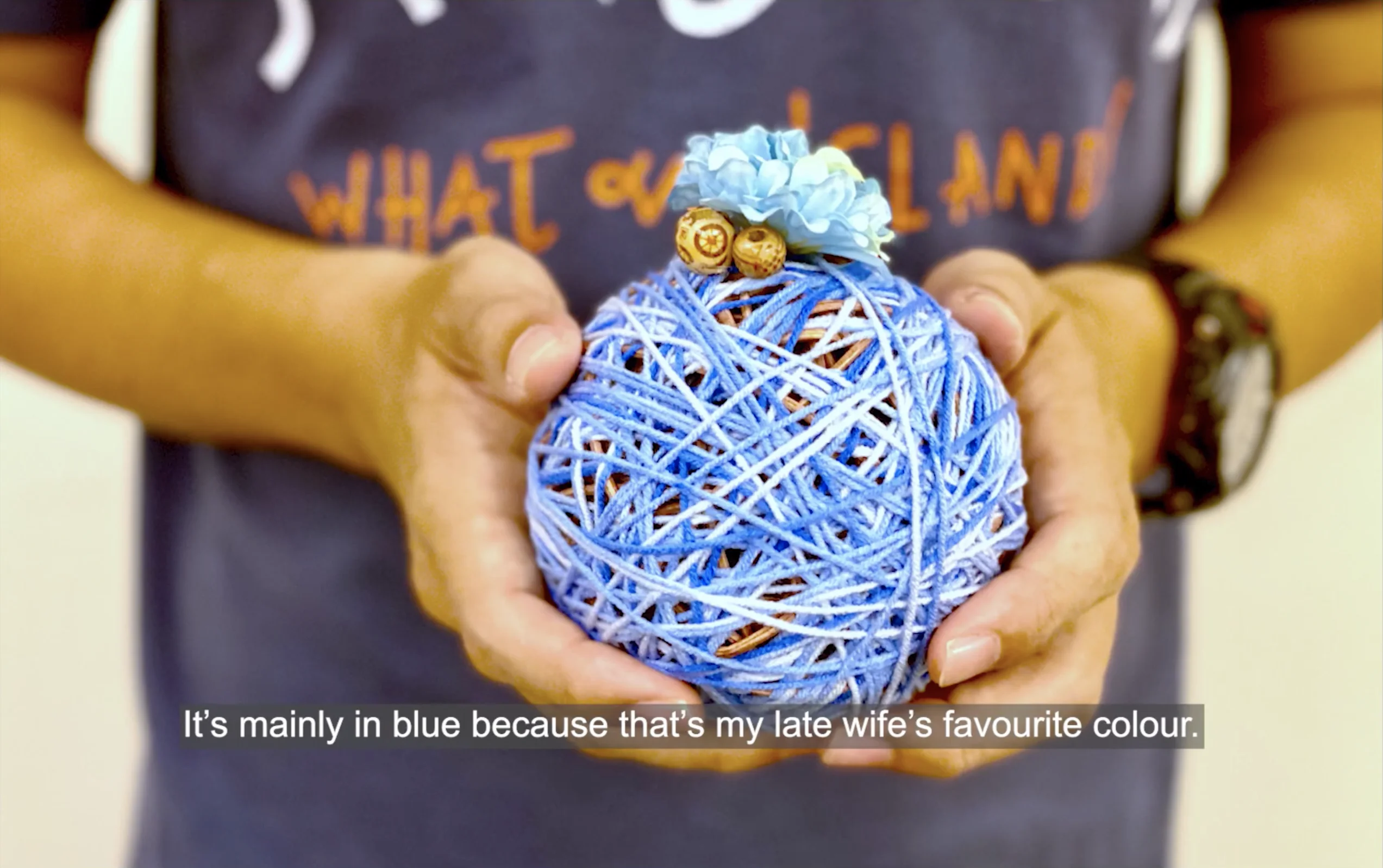 Screencapture from Voices of Grief video. A pair of hands holding a blue remembrance ball.